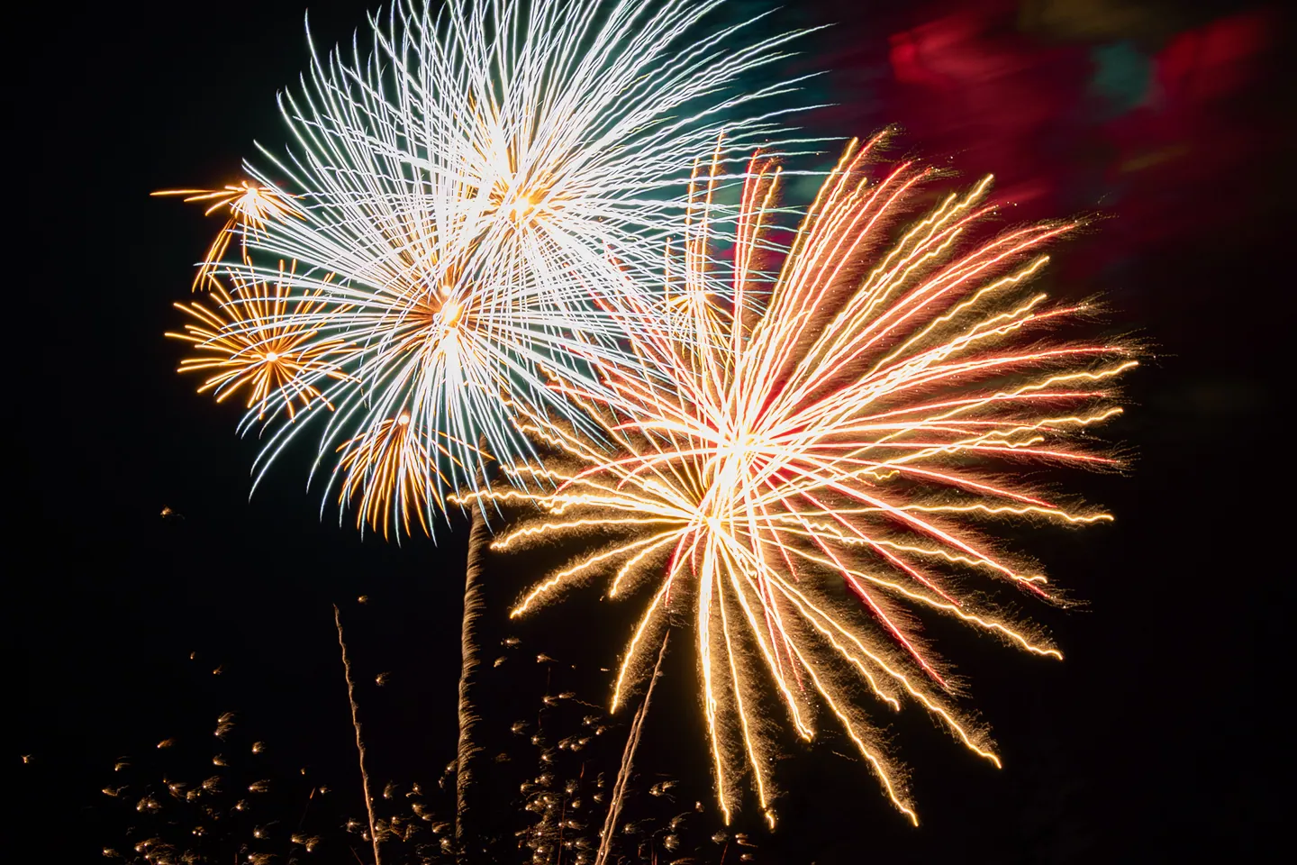 White, gold, and red fireworks blooming against a dark sky